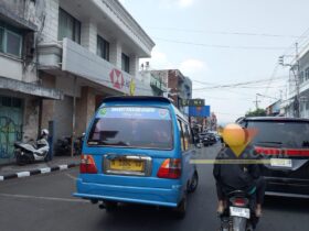 Angkot Pelajar Gratis di Kota Malang Mulai Beroperasi Senin, 90 Unit Disiapkan Kota Malang, blok-a.com – Program angkutan pelajar gratis di Kota Malang direncanakan mulai beroperasi pada Senin (31/8/2026). Dinas Perhubungan (Dishub) Kota Malang kini menyiapkan para pengemudi yang akan terlibat dalam layanan tersebut. Sebelum layanan berjalan, Dishub terlebih dahulu melakukan sosialisasi kepada para pengemudi, termasuk mengenai standar operasional prosedur (SOP) layanan angkutan pelajar gratis. “Konsepnya yang pertama kita lakukan sosialisasi dulu. Yang jelas kita lakukan sosialisasi SOP kepada seluruh pengemudi yang terlibat nanti di layanan angkutan pelajar,” ujar narasumber. Untuk tahap sosialisasi, Dishub sementara mengundang sekitar 60 hingga 70 pengemudi. Namun, jumlah armada yang dibutuhkan untuk menjalankan program tersebut lebih banyak. “Kita membutuhkan 90. Maksimal 90, 90 unit gitu,” jelasnya. Nantinya, tidak seluruh angkot yang disiapkan bisa langsung bergabung. Sebab, masih terdapat sejumlah kendaraan yang harus menyelesaikan proses administrasi dan kelayakan kendaraan, termasuk uji KIR. “Mereka kan butuh Uji KIR juga, ada yang belum,” katanya. Sementara itu, dari sisi perangkat pendukung, sebanyak 73 angkot disebut telah terpasang GPS. Perangkat tersebut menjadi bagian dari sistem pemantauan angkot yang digunakan dalam layanan angkutan pelajar gratis. Jika seluruh persiapan berjalan sesuai rencana, layanan angkot pelajar gratis tersebut ditargetkan mulai berjalan Senin (31/8/2026). “Jalan nanti. Senin insyaallah,” ujarnya. Untuk rutenya, Dishub tidak membuat jalur baru secara keseluruhan. Angkot pelajar gratis akan mengikuti rute yang sebelumnya digunakan bus sekolah. “Rutenya sesuai dengan rutenya bus sekolah,” jelasnya. Saat ini, layanan bus sekolah di Kota Malang memiliki 15 jalur. Rute angkot pelajar gratis nantinya juga akan disesuaikan dengan kebutuhan pelajar, termasuk menjangkau kawasan yang sebelumnya menjadi perhatian dalam layanan bus sekolah. Salah satunya kawasan Madyopuro. Selain itu, wilayah Buring juga menjadi bagian dari cakupan layanan tersebut. “Ya, ditambah lagi tuh. Ya termasuk itu,” katanya. Dengan skema tersebut, angkot pelajar gratis diharapkan tidak hanya mengantarkan pelajar menuju sekolah, tetapi juga memperluas jangkauan layanan transportasi pelajar di sejumlah kawasan Kota Malang.